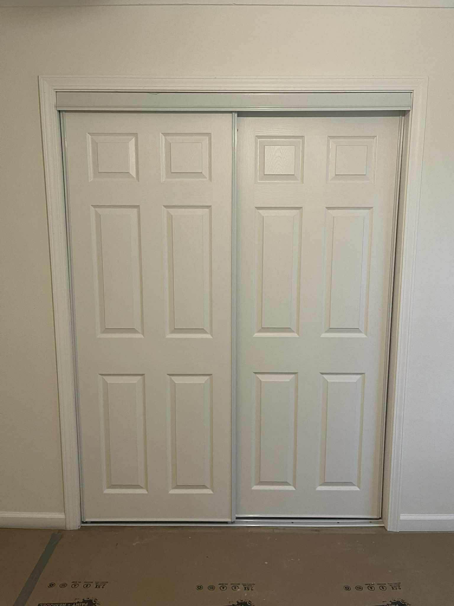 Bypass closet door installation with white six-panel doors and aluminum track