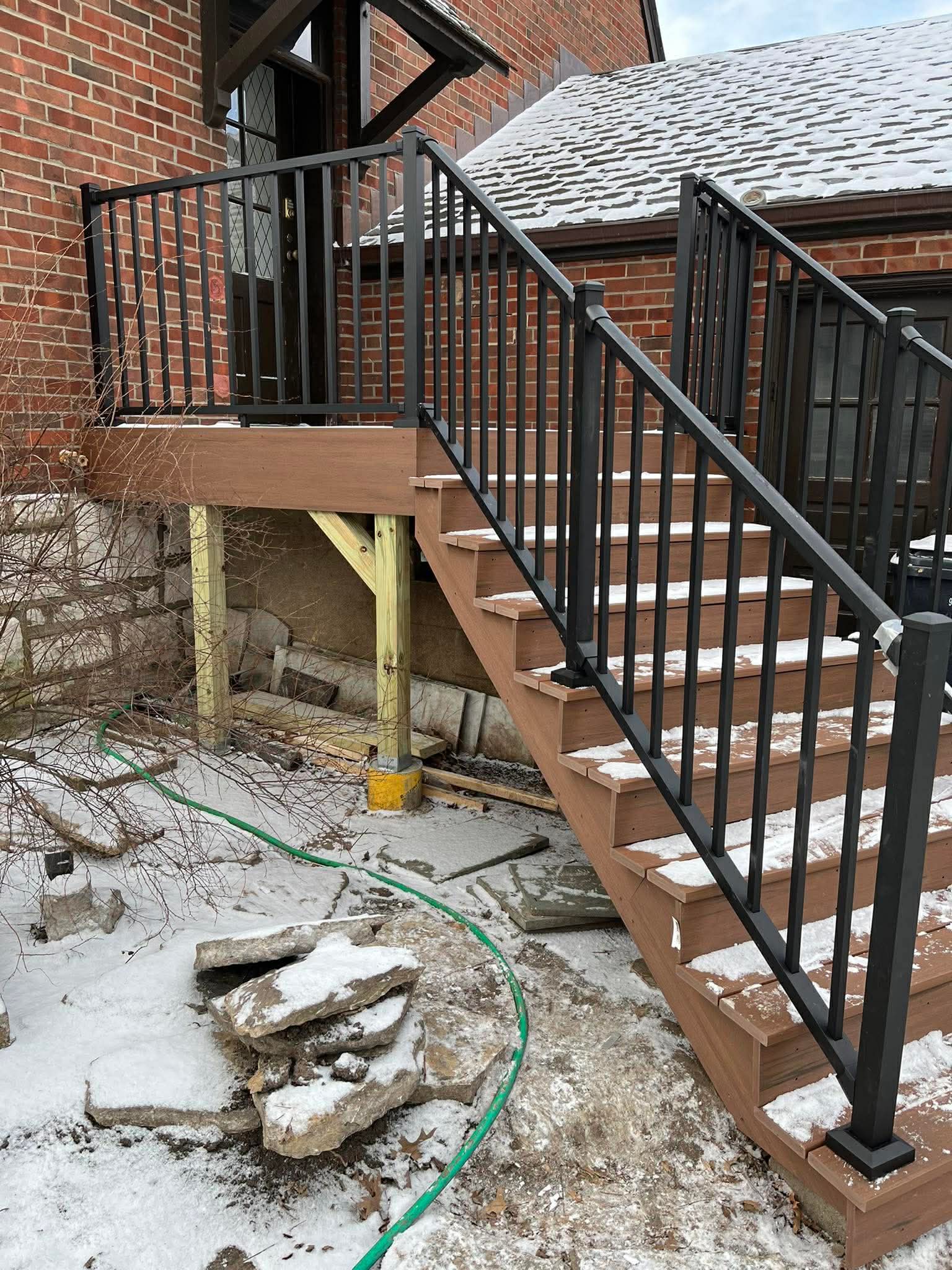 Composite deck staircase with black aluminum railing installed on brick home exterior