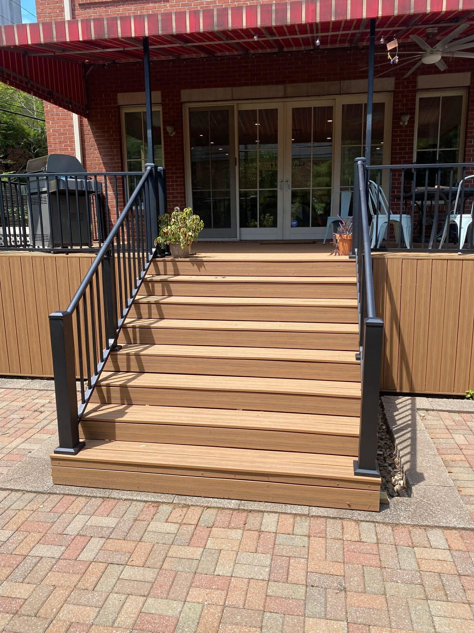 Composite deck stairs leading to paver patio with retractable awning and black metal railing