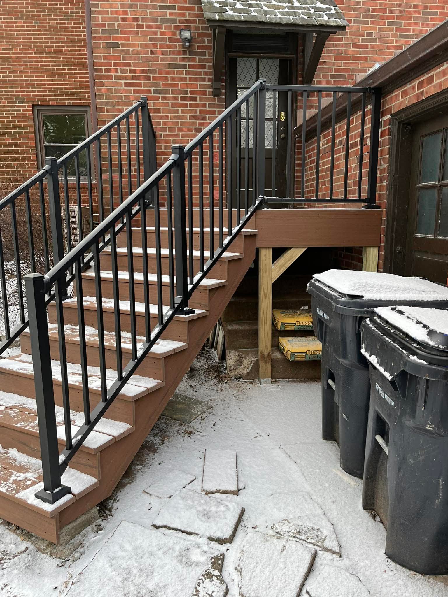 Side entry deck staircase with composite treads and black metal railing on brick home