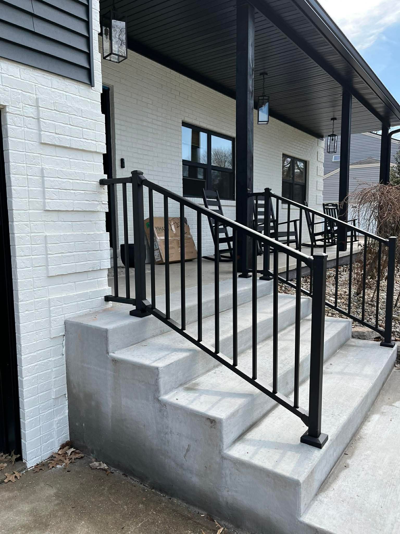 Concrete porch steps with black metal railing and modern front entry on white brick home