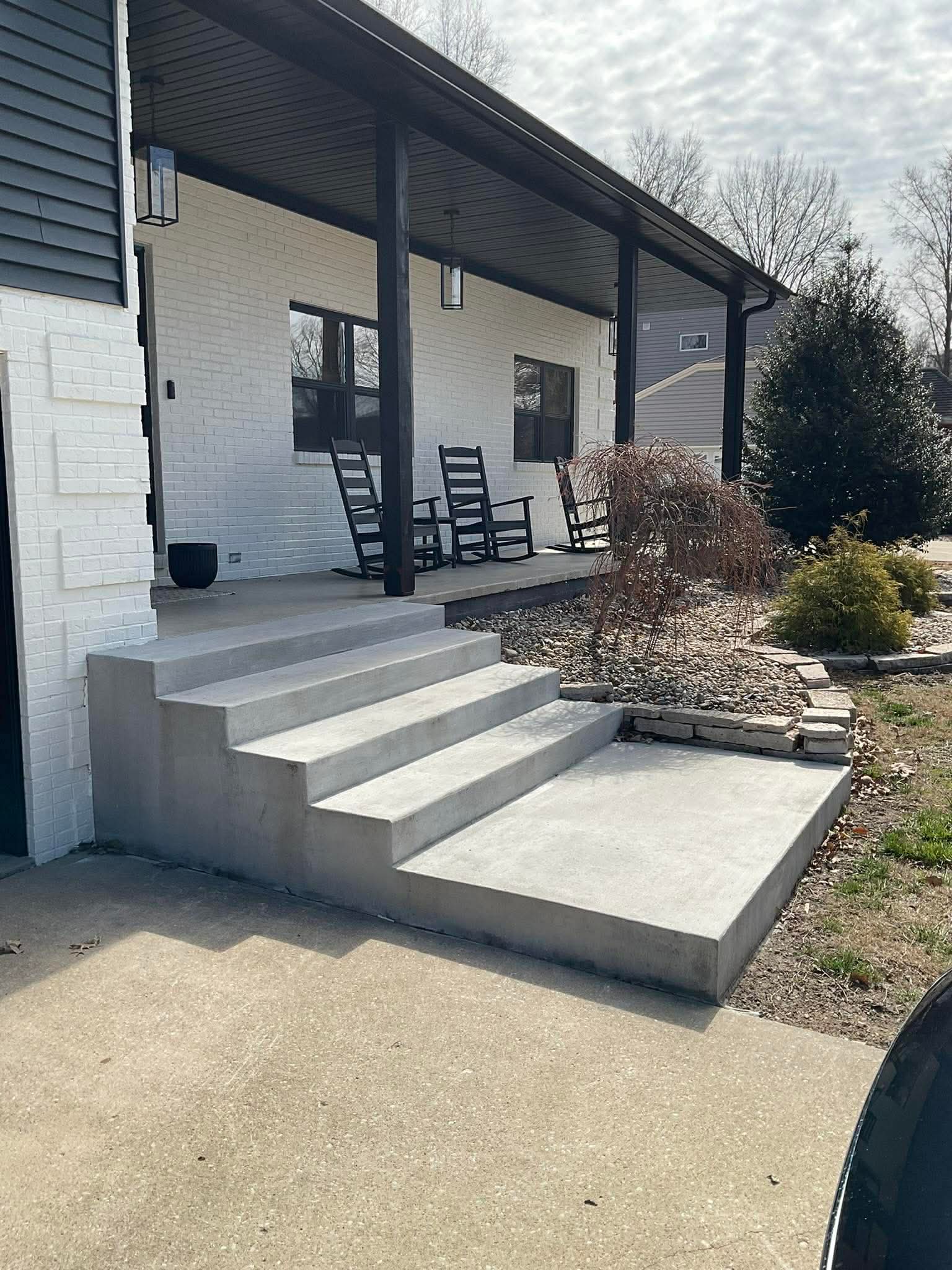 New concrete porch and steps on white brick home with dark trim and covered porch