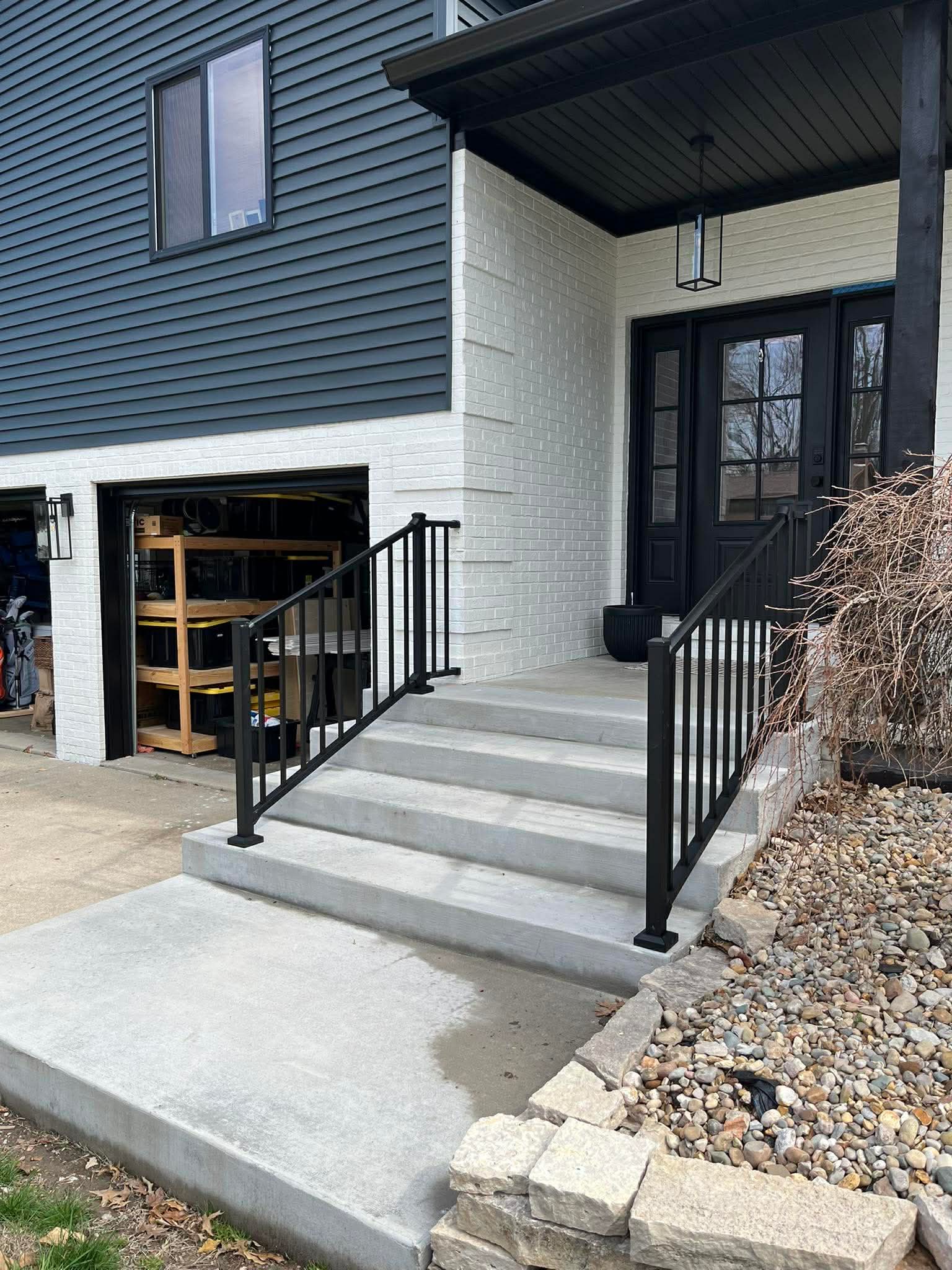Front entry concrete steps with black aluminum railing and landscaping rock border