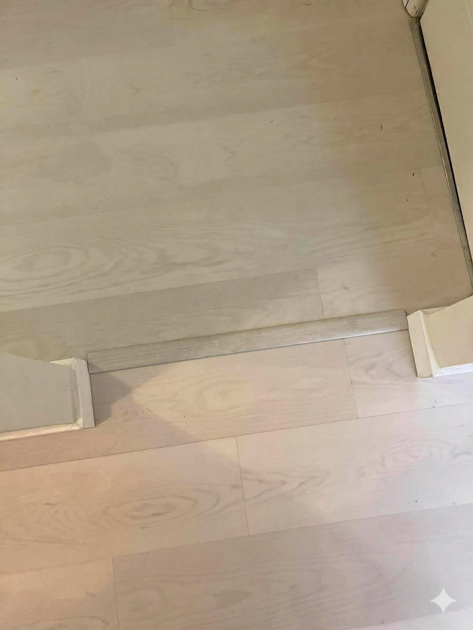 Light maple luxury vinyl plank flooring with doorway transition strip and white baseboard trim installed by Frame to Finish