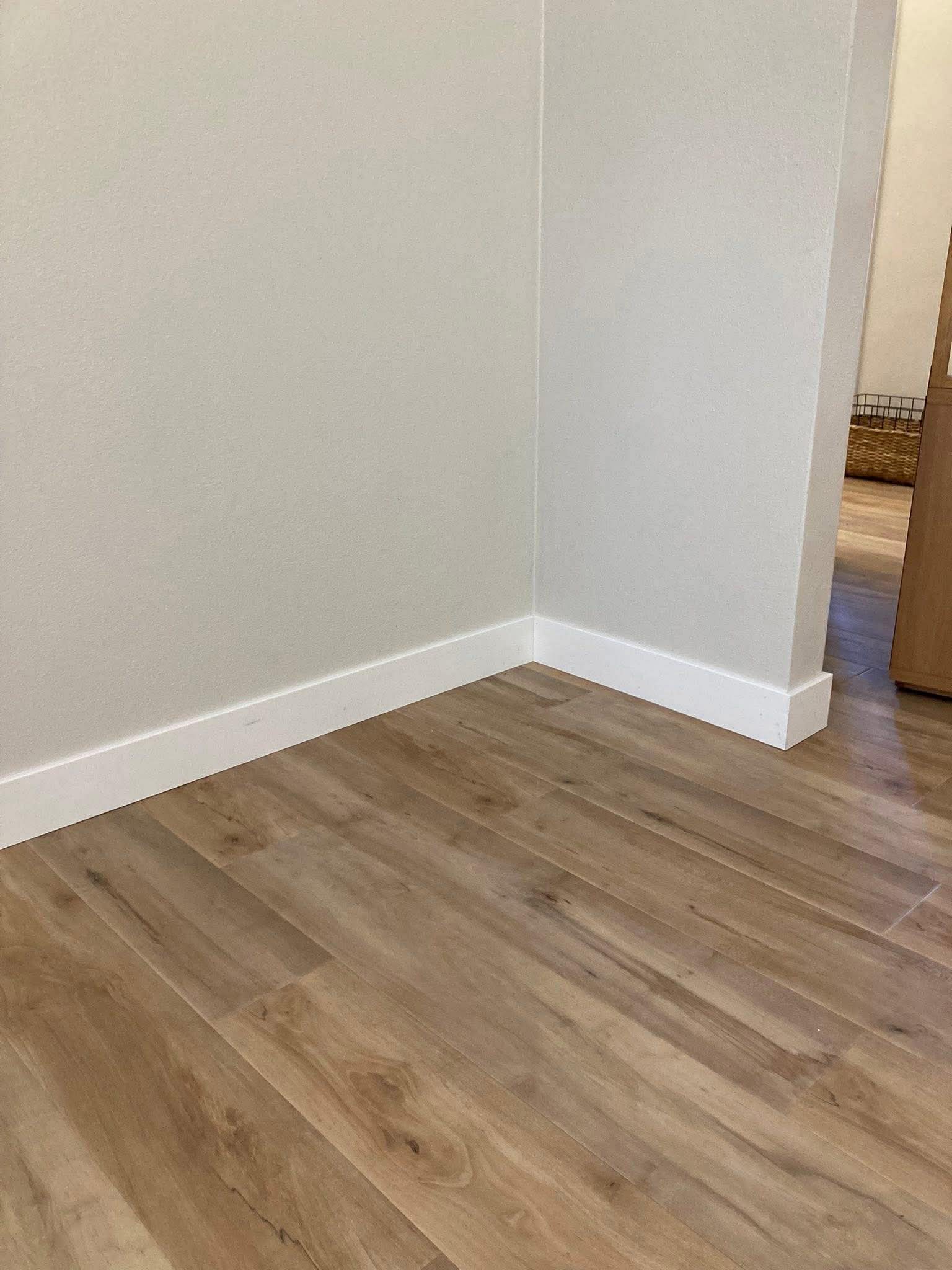 Light oak luxury vinyl plank flooring with clean white baseboard trim installation