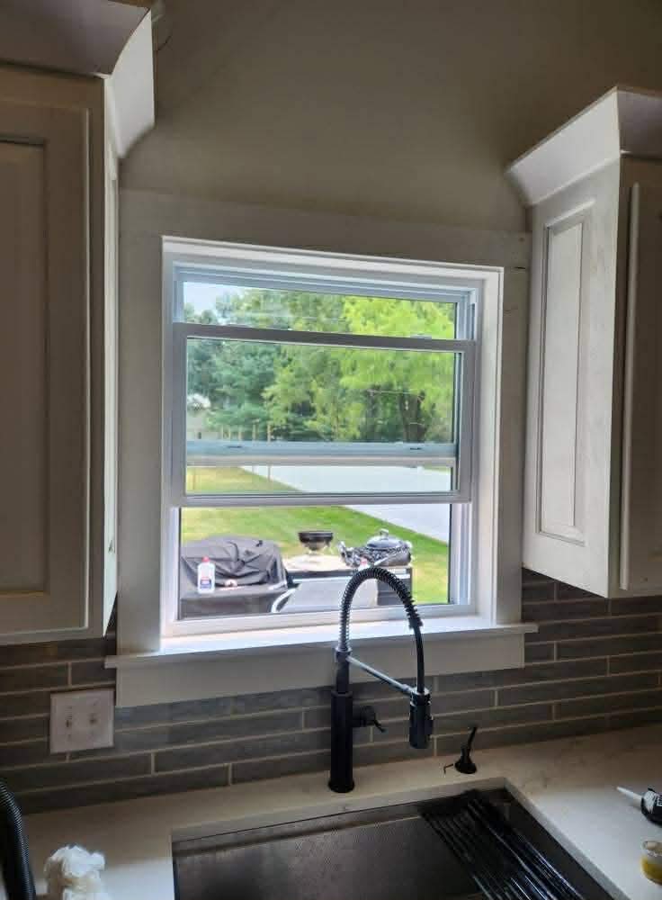 Kitchen sink area with stone backsplash, custom window trim, and white cabinetry in Belleville IL home