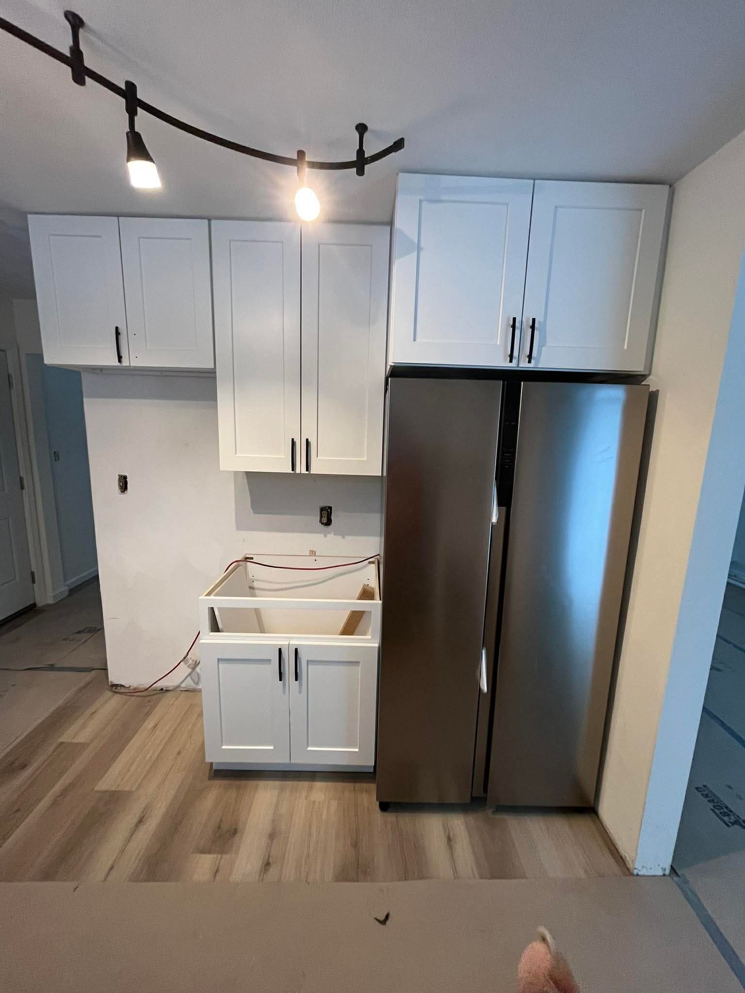 White shaker cabinet installation with stainless steel refrigerator and track lighting